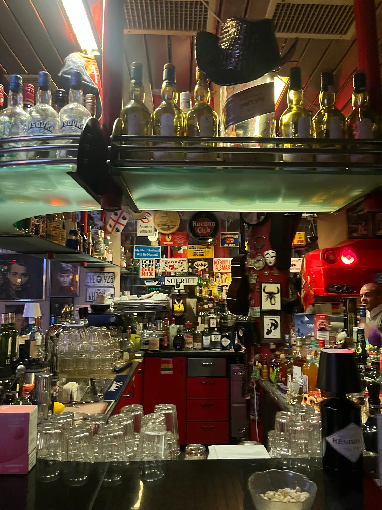 Blick über den Tresen von Sherif’s Bar: Flaschen im Regal, ein schwarzer Cowboyhut, Emailschilder, ein Schild mit der Aufschrift Sheriff und rote Schränke
