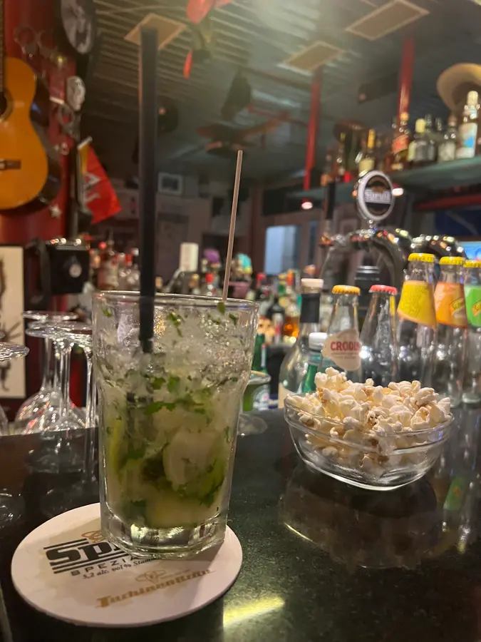 Mojito mit viel Minze und Eis, daneben eine Schale Popcorn auf dem Tresen