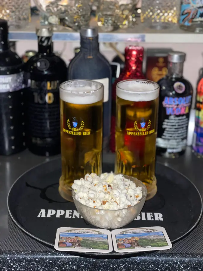 Zwei Gläser Appenzeller Bier mit Popcorn vor einem Regal voller Wodkaflaschen